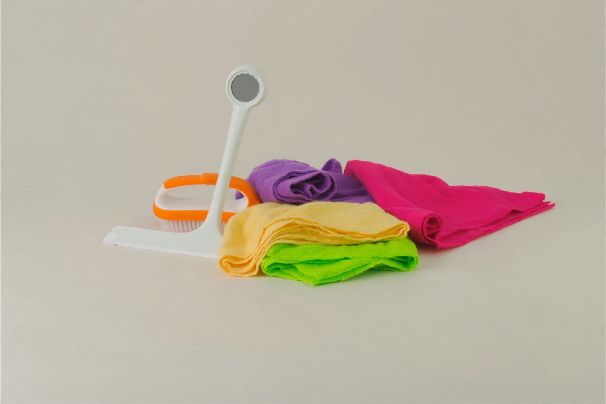 Overhead flat-lay of neatly arranged cleaning tools and folded microfibre cloths on a plain surface