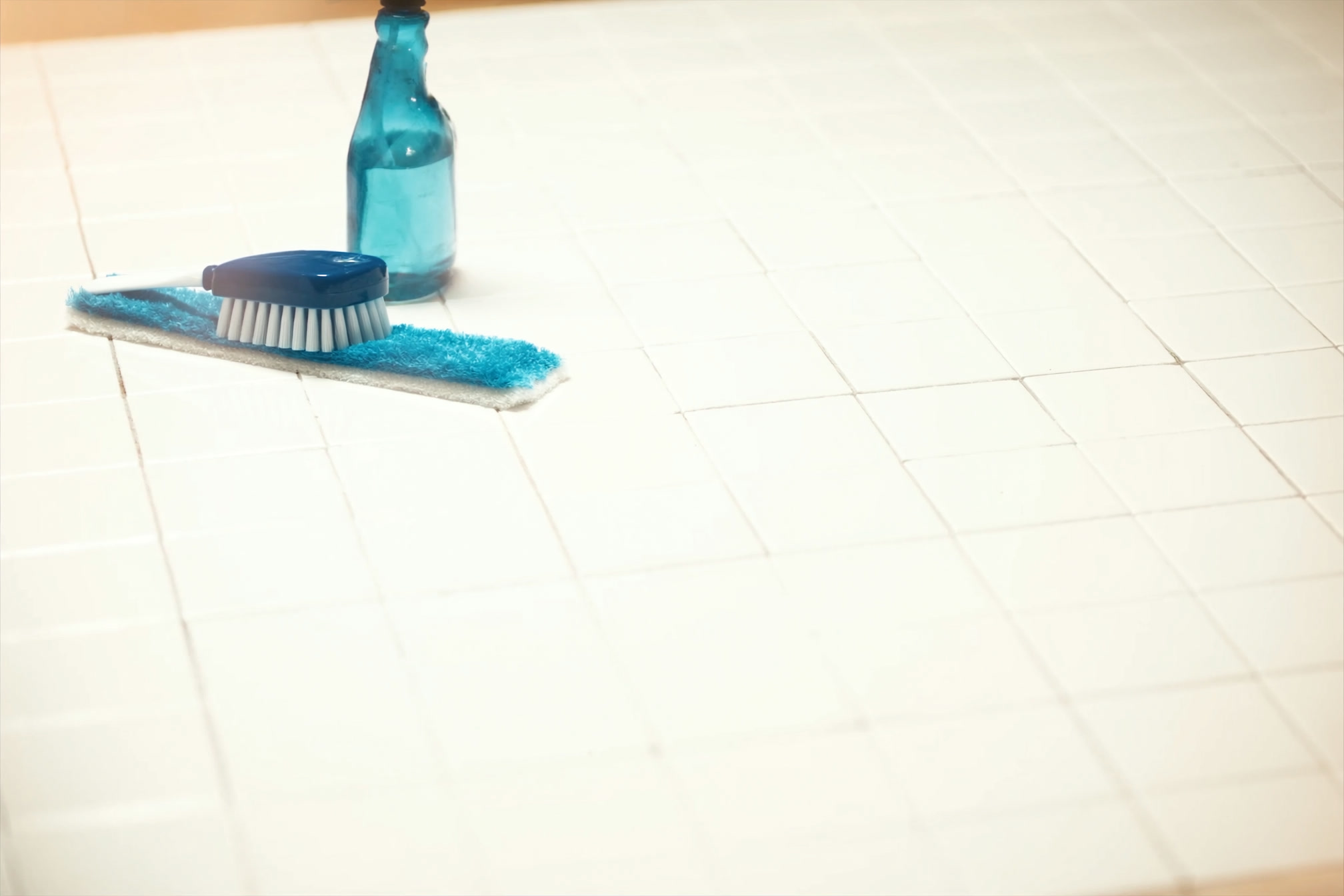 Close detail of bathroom tile and grout being cleaned with a brush and spray bottle, high-key light