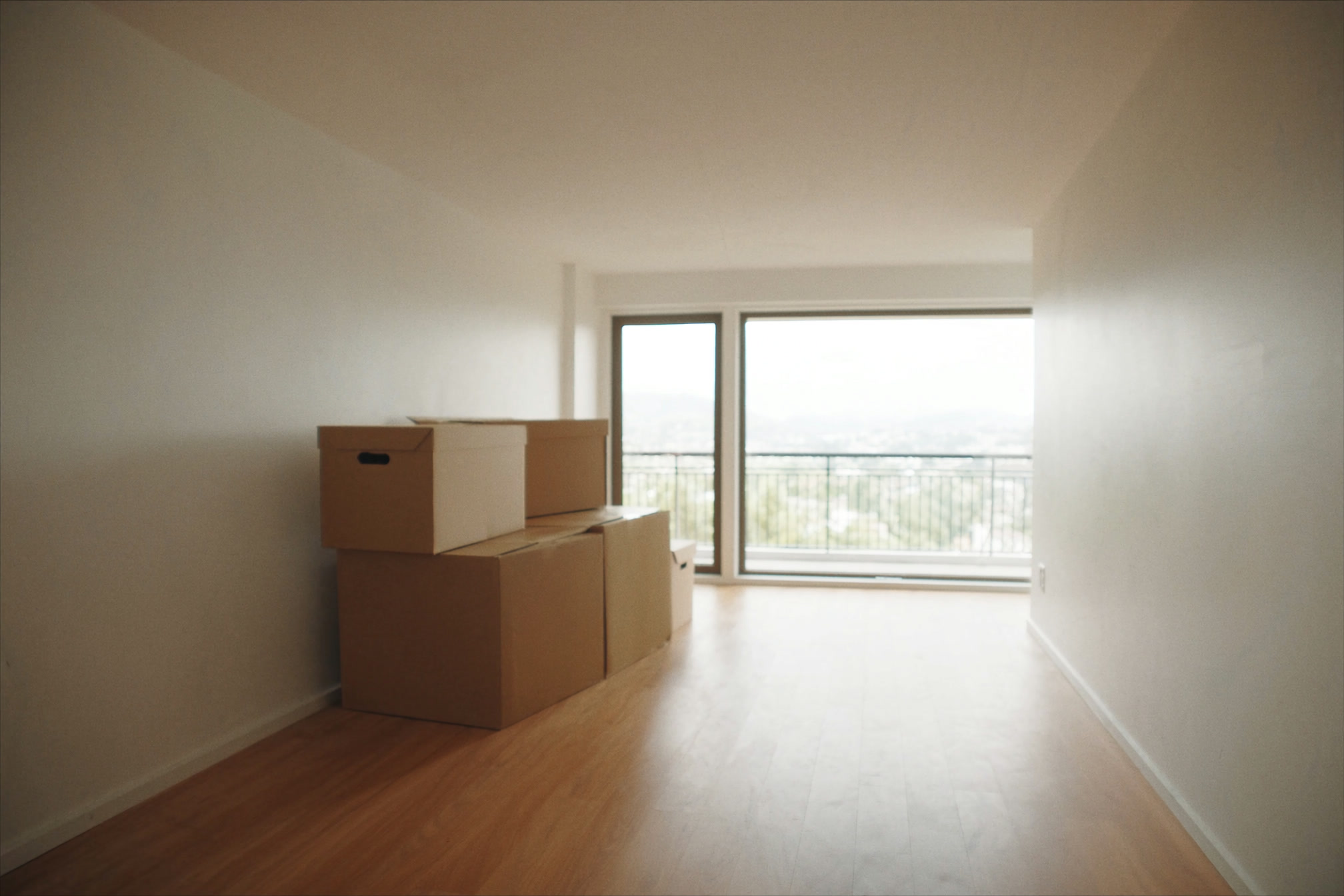 Empty apartment interior with clean bare floors and a few closed moving boxes by the wall, window light